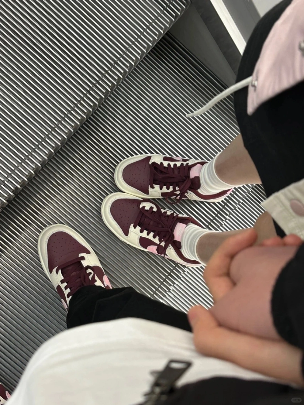 Cặp đôi nắm tay tình tứ trên thang cuốn diện giày đôi sneaker tông màu đỏ trắng cá tính