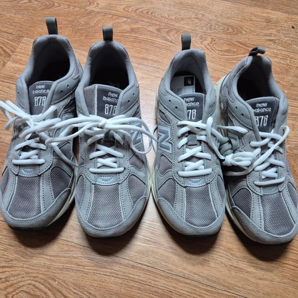 Hai đôi giày đôi New Balance màu xám ghi cổ điển đặt trên nền gỗ sang trọng