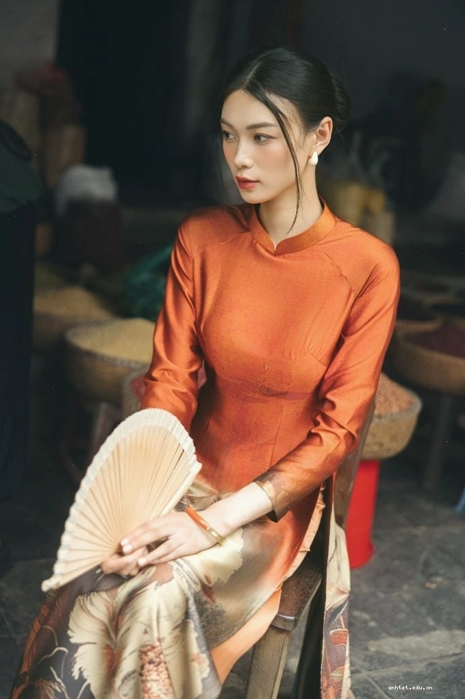 Áo dài in hoa, cổ tròn, tay lỡ, gam màu cam đất, họa tiết hoa văn nhỏ, mang vẻ đẹp ấm áp, dịu dàng.