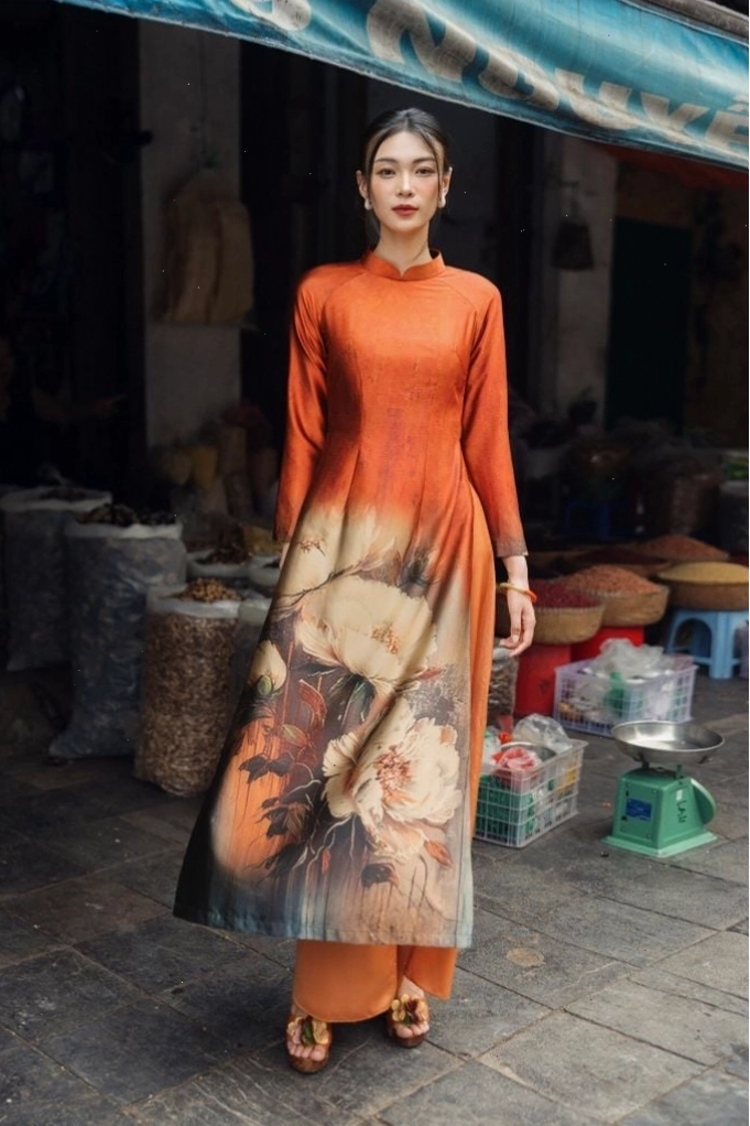 Áo dài in hoa, cổ tròn, tay lỡ, gam màu trắng, họa tiết hoa văn lớn màu đỏ và xanh, mang vẻ đẹp nổi bật, ấn tượng.