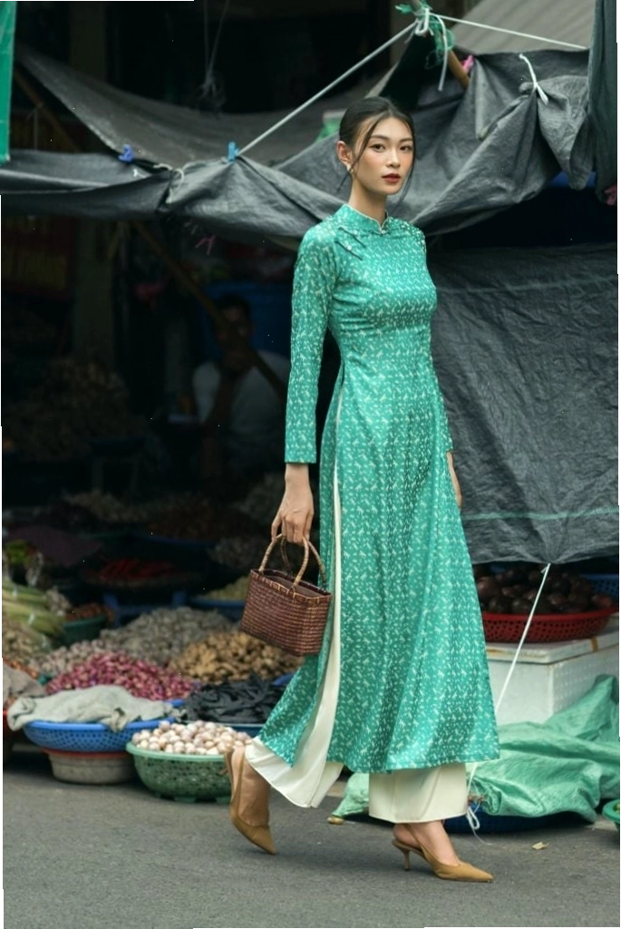 Áo dài lụa xanh ngọc, cổ tròn, tay lỡ, họa tiết thêu hoa trắng nhỏ, chi tiết cách điệu ở tà áo, mang vẻ đẹp bay bổng, duyên dáng.