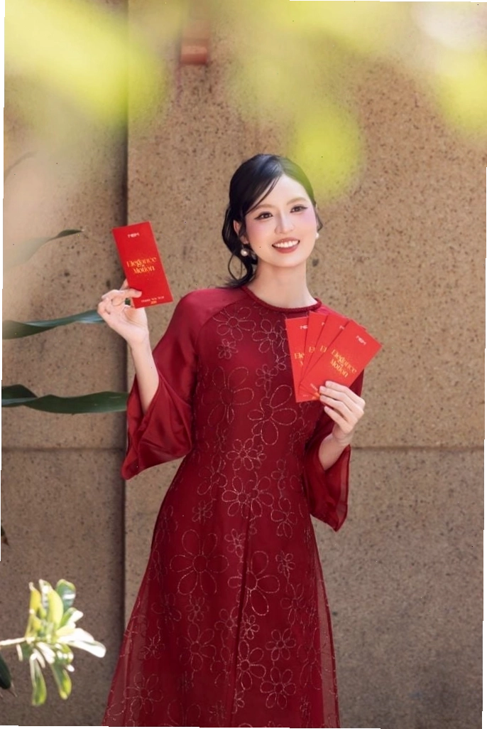 Áo dài thêu hoa trên nền vải hồng pastel, cổ tròn, tay lỡ, tôn lên vẻ dịu dàng và nữ tính.