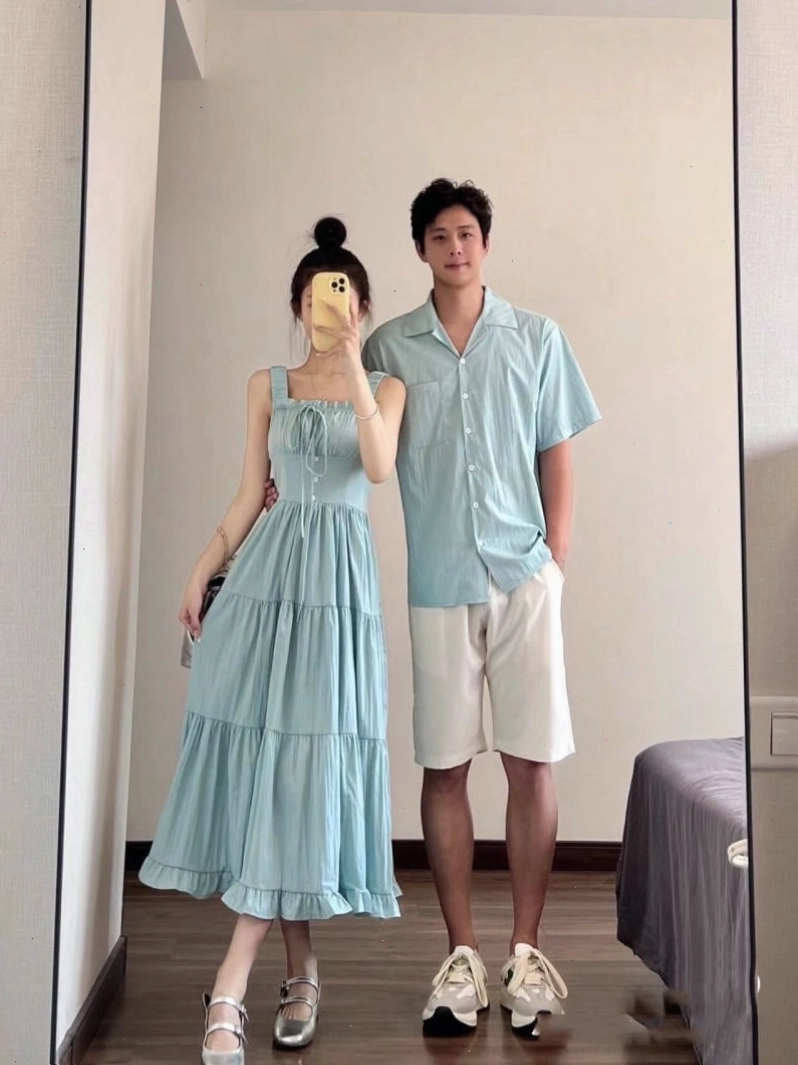 Cặp đôi chạy nô đùa trên bãi biển, té nước vào nhau, mặc đồ đôi đi biển màu trắng