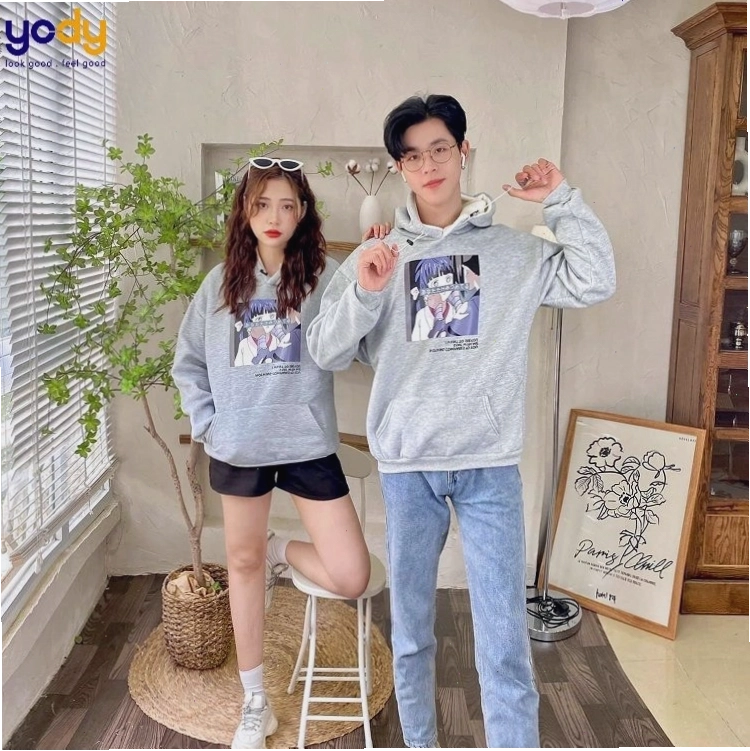 Cặp đôi mặc áo hoodie đôi màu nâu và be, quần kaki, tạo dáng nhìn xa xăm