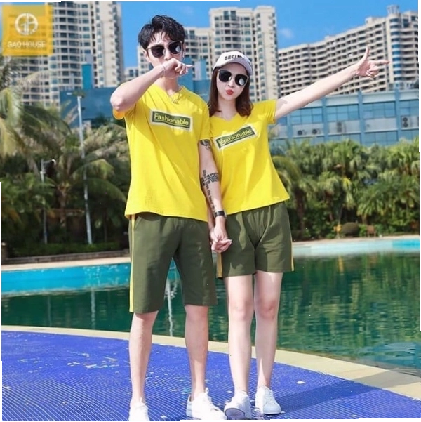 Cặp đôi mặc áo thun có in chữ nhỏ ở ngực, tạo dáng nhìn nhau cười, nắm tay nhau