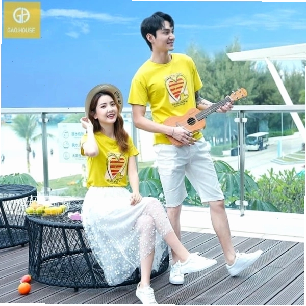 Cặp đôi mặc áo thun trắng in hình trái tim cách điệu, quần short, tạo dáng nhìn nhau cười