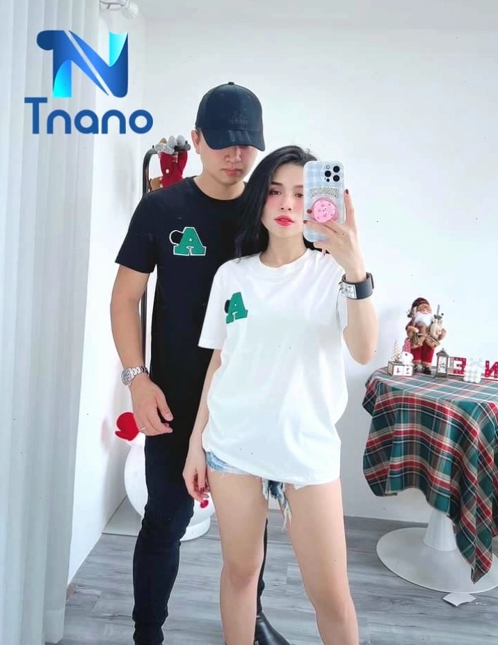 Cặp đôi mặc áo thun trơn màu be và quần đen, tạo dáng dựa vào nhau