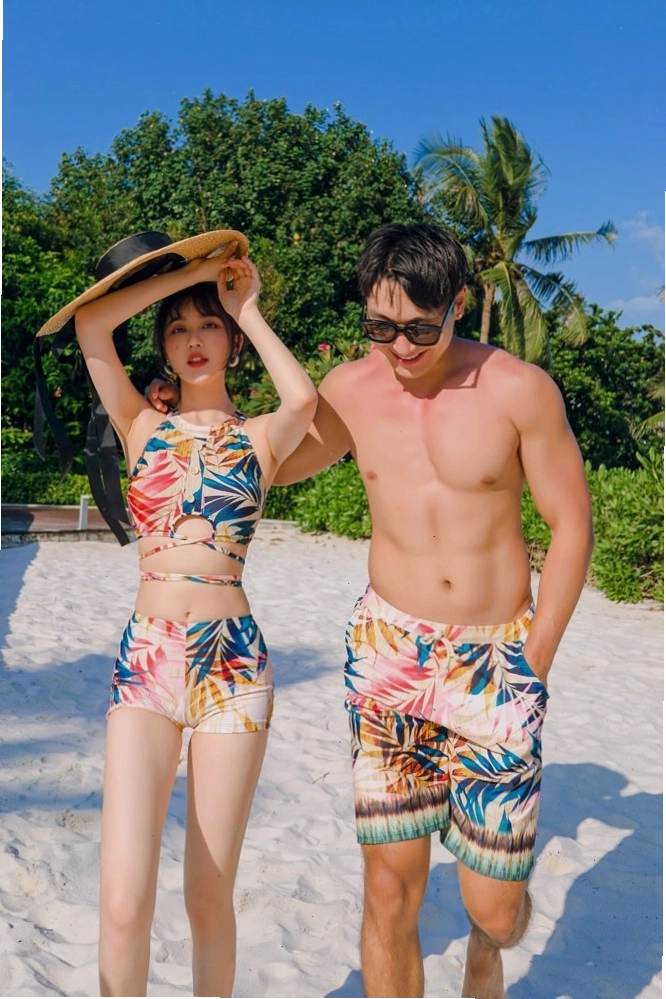 Cặp đôi mặc quần đôi đi biển màu xanh dương và trắng, tạo dáng nắm tay nhau trên bãi cát