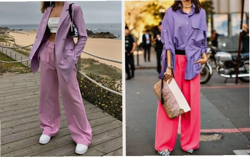 Cặp đôi mặc trang phục màu tím pastel và tím đậm, tạo dáng dựa vào nhau trên nền tường trắng.