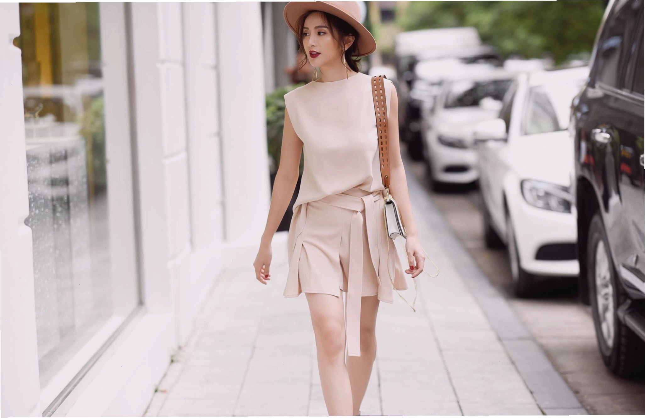 Cô gái diện chân váy công sở ngắn màu be cùng áo len mỏng và túi xách