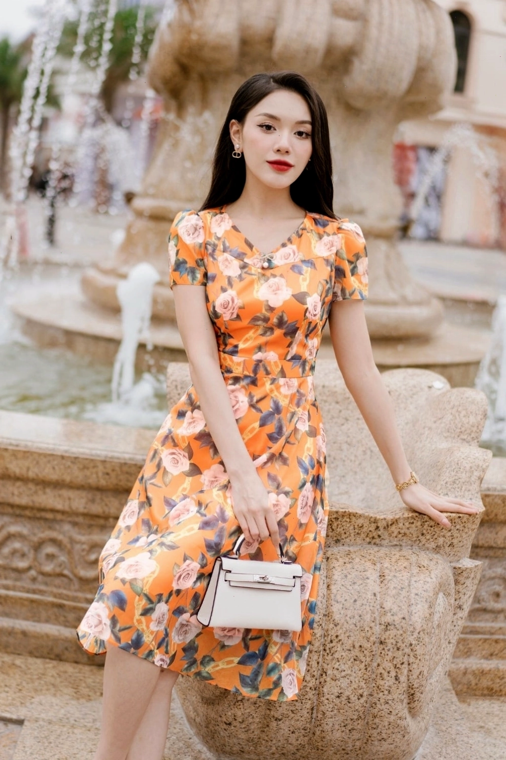 Đầm maxi dáng dài họa tiết hoa to màu vàng cam, cổ yếm buộc dây, thân trên ôm nhẹ, chân váy xòe rộng tạo hiệu ứng bay bổng.