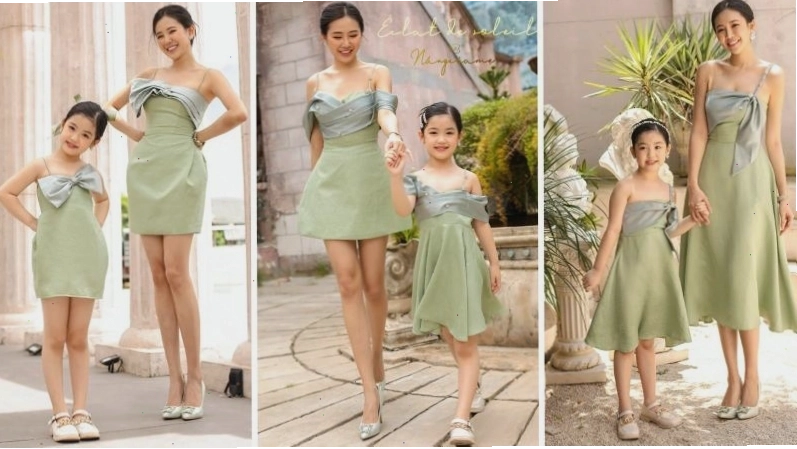 Mẹ và bé gái cùng mặc váy họa tiết hoa nhí màu vàng, tạo dáng tung váy trên bãi biển