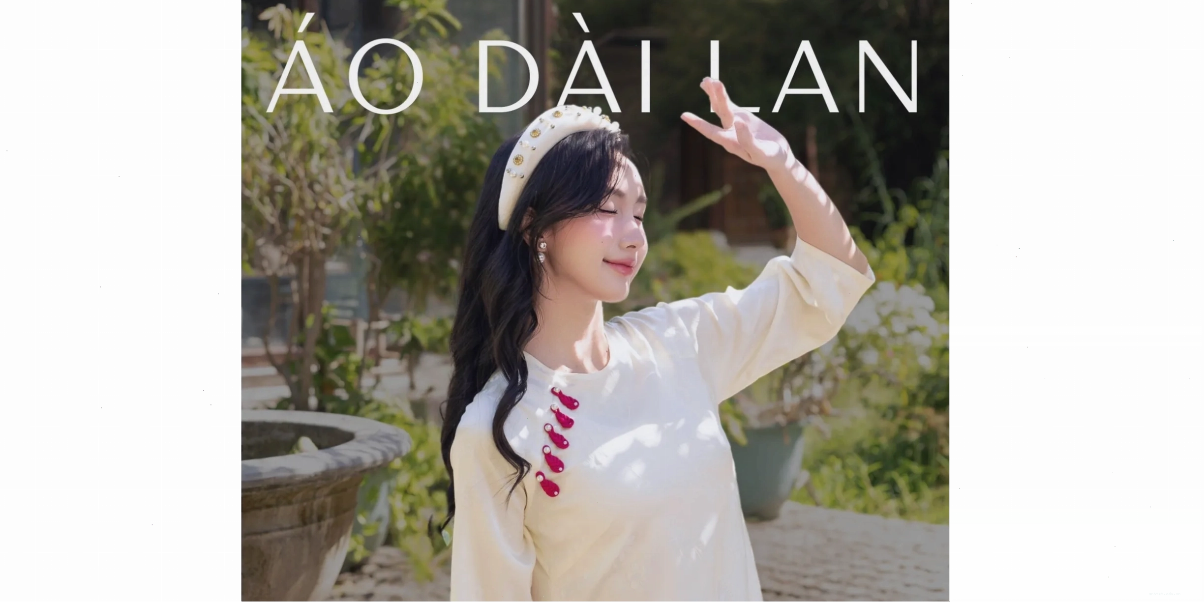 Người mẫu diện áo dài cổ thấp lụa gấm màu xanh ngọc bích, tay phồng nhẹ, phối cùng quần lụa trắng ống rộng và túi xách kẹp nách.