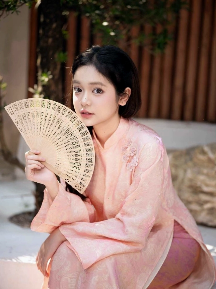 Người mẫu diện áo dài gấm đỏ với họa tiết dập chìm sang trọng, cổ cao kín đáo, tay lỡ thanh thoát.